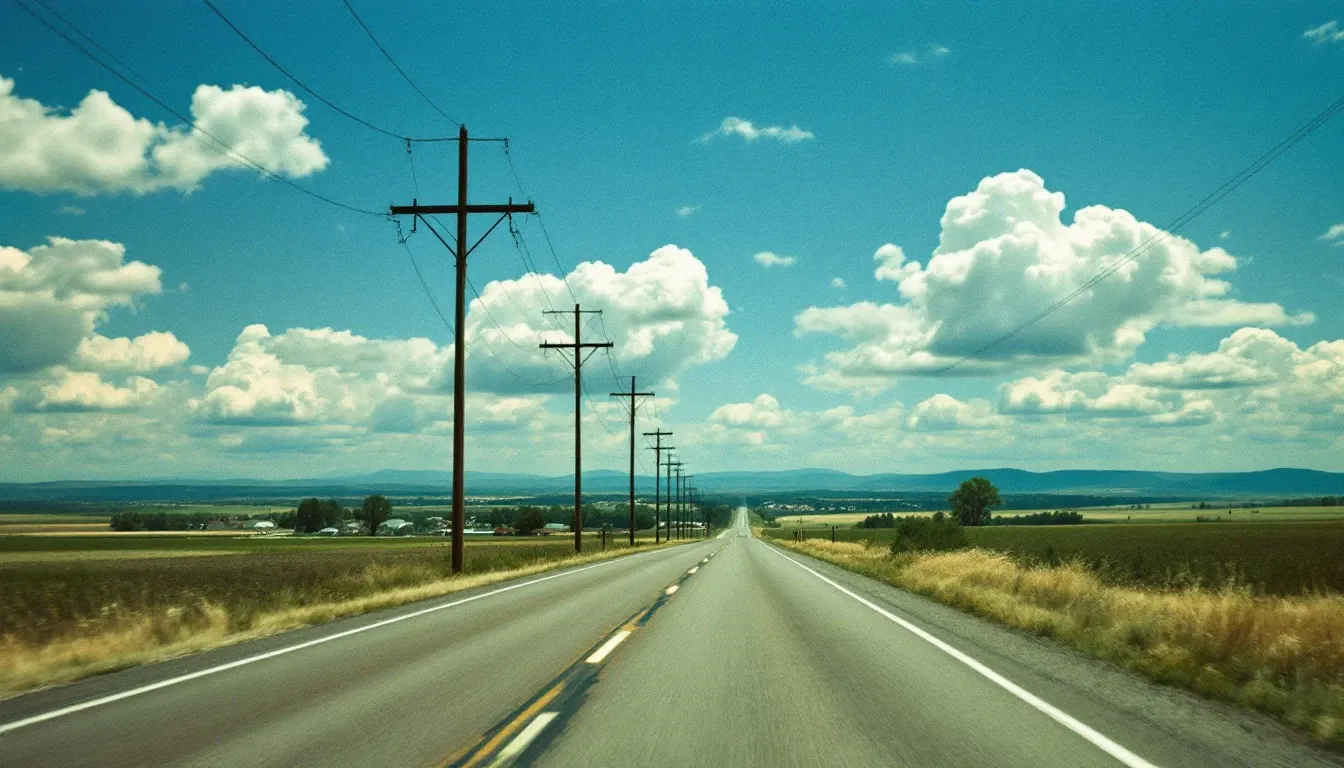 A two-lane rural American road running to the horizon, distribution poles along the verge.